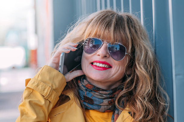 portrait of smiling blonde woman talking on mobile phone in the street - Photo, Image
