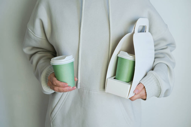 Holder of a cardboard box for coffee cups in the hands of a girl. Time to drink coffee or tea. White cardboard stand for takeaway coffee cup. Delicious hot beverage. Disposable paper cup. Blank space - Foto, Imagem
