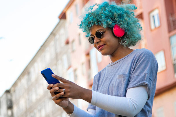 afro amerykańska dziewczyna uśmiechnięta ze słuchawkami i telefonem komórkowym w mieście - Zdjęcie, obraz