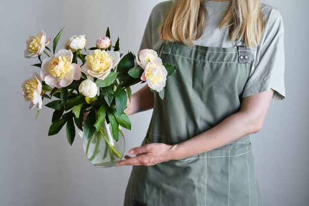 Peonies in the hands of a happy woman. Stylish white peonies in florist hand. The florist girl gathered a bouquet. Beautiful spring gentle flowers. Gift for the holiday. Fresh floral. Blossom petal - Фото, изображение