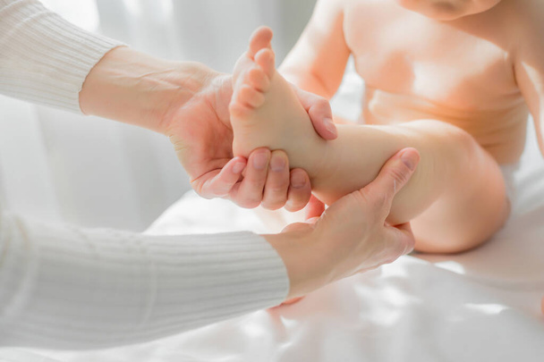 Mom gives her baby a leg and foot massage. Close-up. - 写真・画像