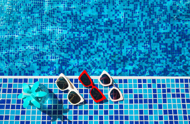Cóctel fresco con paja y una selección de tres gafas de sol diferentes junto a la piscina. Concepto de vacaciones y viajes. Fondo del complejo tropical. - Foto, imagen