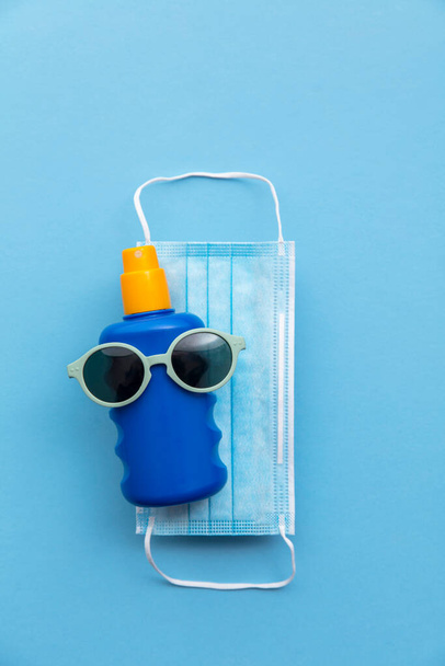 Coronavirus summer vacation background. Sun cream with sunglasses and face mask - Foto, Imagem