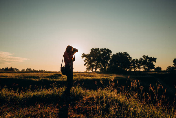 silhouette woman traveler with camera takes pictures of landscape with hills beautiful sunset - Zdjęcie, obraz
