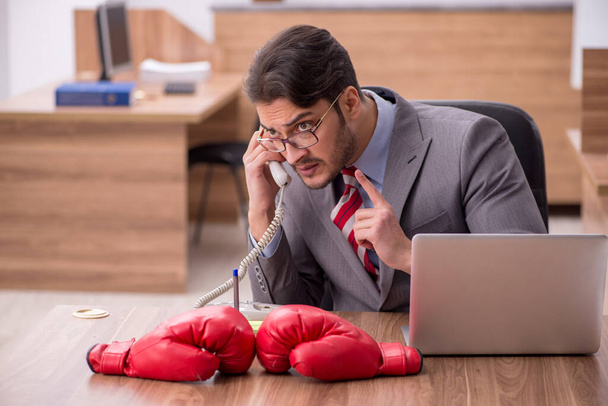 Joven empleado masculino usando guantes de boxeo en el lugar de trabajo - Foto, imagen