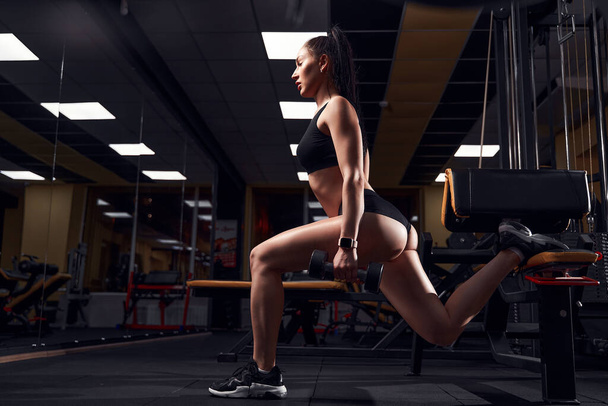 Slim fit woman doing lunges with dumbbells in her hands in a modern gym - Φωτογραφία, εικόνα