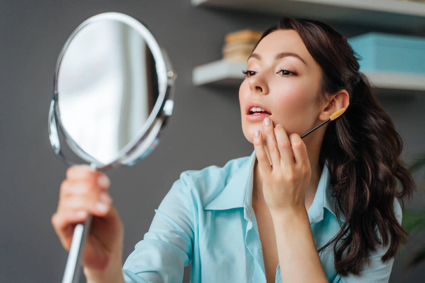 Joven bonita mujer hace maquillaje en casa mientras se mira en el espejo - Foto, Imagen