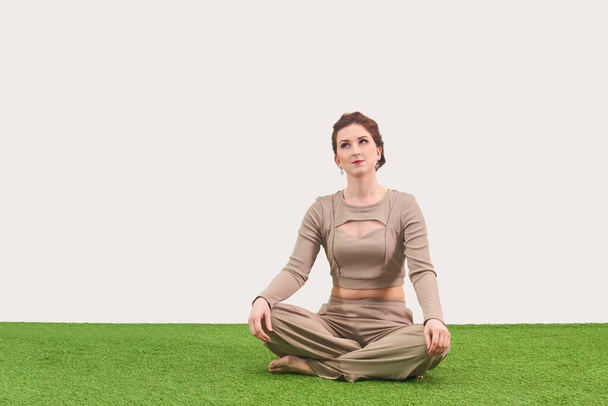 mujer joven sentada en posición de loto para meditar y mira hacia arriba soñando sobre fondo claro - Foto, Imagen