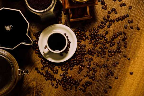 Kawa. Widok z góry na biały kubek z czarną kawą, włoski ekspres do kawy moka, młyn i ziarna na drewnianym stole. Vintage stylu rustykalnym. - Zdjęcie, obraz
