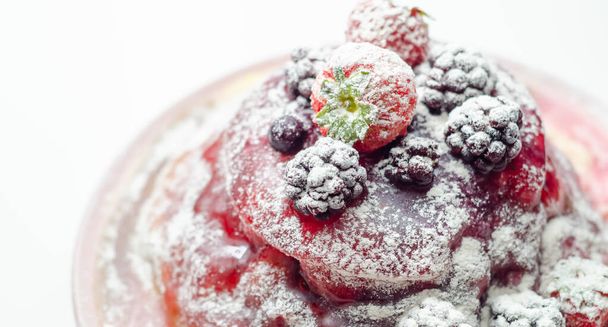 Pancakes stack with strawberries, blueberries, and blackberries, topped with sauce and sprinkled with powdered sugar, sweet breakfast - Photo, image