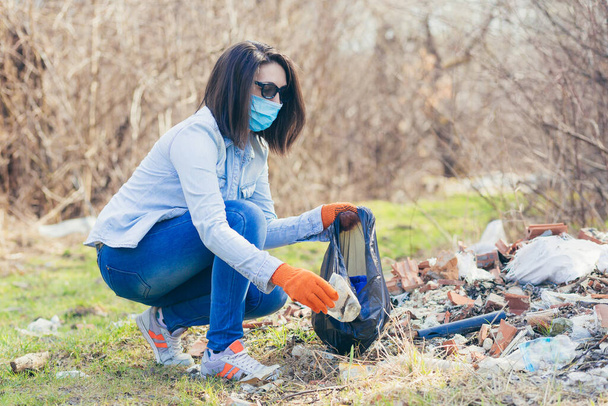 Young beautiful female volunteer collects plastic garbage in the forest and park, volunteer holding a bag with collected plastic and garbage - Фото, зображення