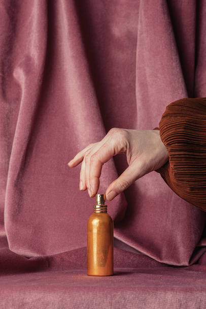 Kobieta trzyma złotą butelkę perfum na tle bordowy kolor tkaniny  - Zdjęcie, obraz