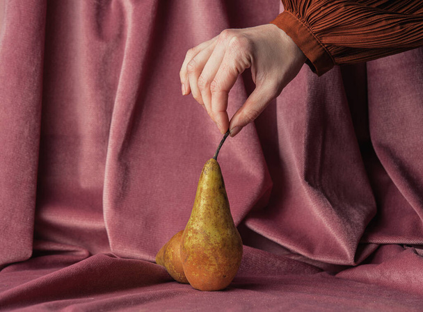 Female hold pear on burgundy color fabric background  - Zdjęcie, obraz