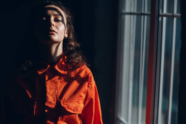 Young brunette curly woman in orange suit. Female in colorful overalls portrait. - Фото, зображення