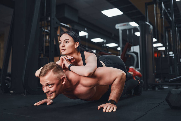 Young muscular man doing push-up exercise and holding girl. joint training. Group lessons. Teambuilding. romance. - Fotoğraf, Görsel