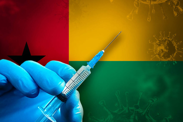Кампания по вакцинации против гепатита Ковида-19. Рука в синей резиновой перчатке держит шприц с вирусной вакциной ковид-19 перед флагом Гвинеи-Бисау. Концепция вакцинации коронавируса - Фото, изображение