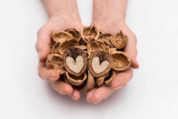 Woman holds out her hands with a bunch of peeled shell and two halves of a walnut in the form of a heart on a white background, isolated. Nut concept. - Foto, Imagen