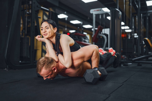 Young muscular man doing push-up exercise and holding girl. joint training. Group lessons. Teambuilding. romance. - Foto, afbeelding