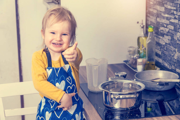 Słodki uśmiechnięty chłopczyk pokazuje palec przed kamerą w kuchni. Poziomo.  - Zdjęcie, obraz