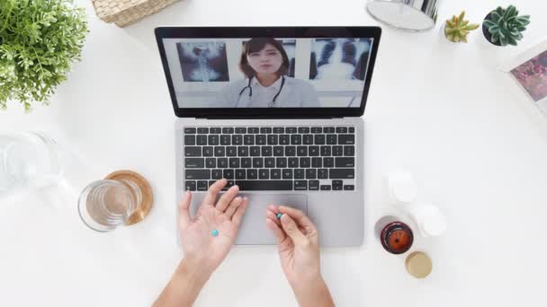 コンピュータのラップトップを使用している若い女性のトップビューは、自宅のリビングルームでアジアの医師オンライン相談とのビデオ会議コールで病気について話します。社会的距離コロナウイルスの隔離. - 映像、動画