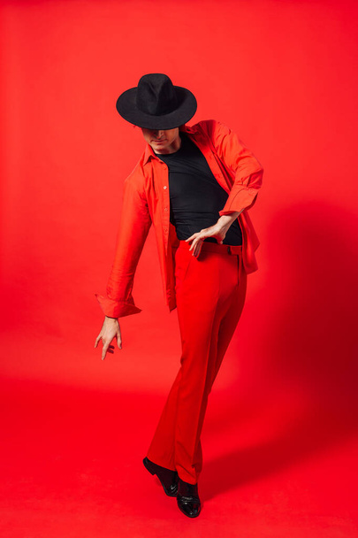 Portrait of a tall handsome man dressed in red shirt and black hat posing on the red background. - Foto, afbeelding