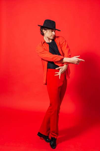 Portrait of a tall handsome man dressed in red shirt and black hat posing on the red background. - Foto, imagen