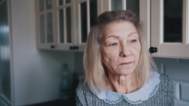 Triste vecchia donna dai capelli grigi che guarda attraverso la finestra. Persona vulnerabile in quarantena - Filmati, video