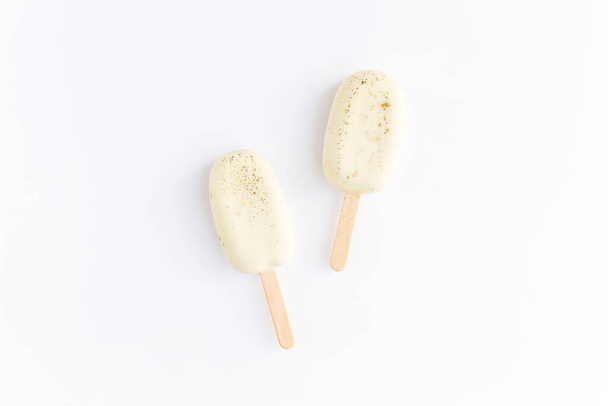 Witte koekjesijsjes op een stokje op witte achtergrond. Vlak gelegd met geïsoleerde ijsjes.  - Foto, afbeelding