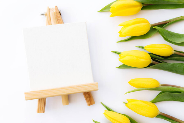 Flat lay with yellow tulip flowers and empty picture frame on white background. Greeting card design for Easter, Mothers day, International womens day or Saint Valentines day - Photo, Image