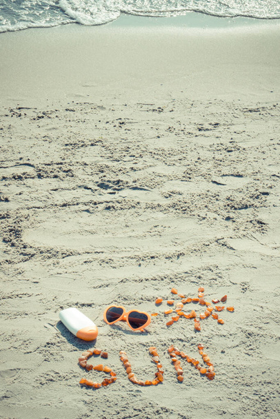 Vintage photo, Inscription and shape of sun made of amber stones, sunglasses and sun lotion on sand at beach, concept of sunbathing, summer and vacation time - Foto, Imagen