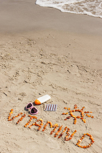 Medical pills, inscription vitamin D made of amber stones and accessories for sunbathing, concept of prevention of vitamin D deficiency, copy space for text on sand at beach - Foto, Imagen