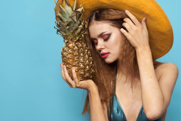 mujer en playa sombrero piña celebración traje de baño frutas exóticas fondo azul vacaciones - Foto, imagen