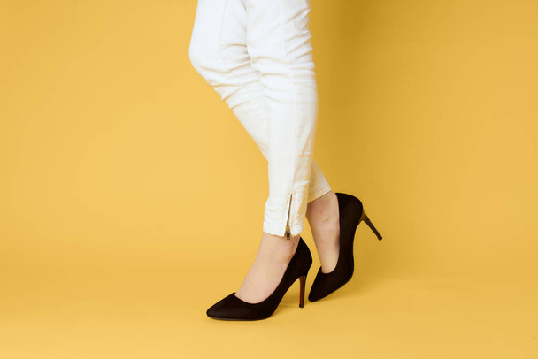 Woman in black shoes legs clipped lit yellow background fashion shopping - Foto, afbeelding