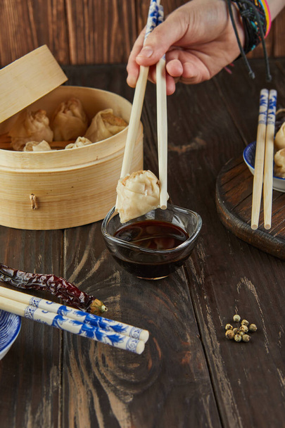 Shumai shaomai albóndigas de carne china al vapor en un vapor de bambú. Mano con palillos sosteniendo dim sum. - Foto, imagen