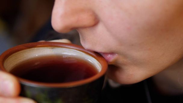 Woman blows on black tea and dinks it from ceramic tea cup. Art of tea concept - Φωτογραφία, εικόνα
