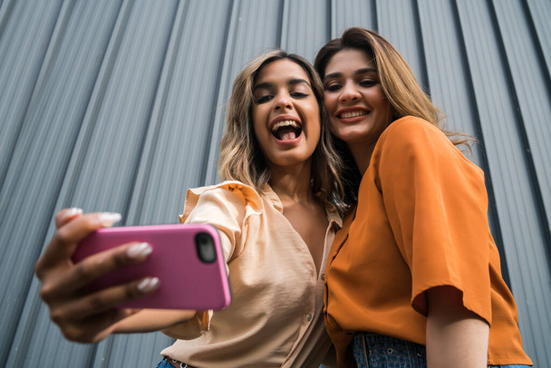 Two friends taking selfie with phone outdoors. - Фото, зображення