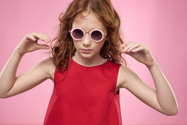 Dziewczyna z kręcone włosy ciemne okrągłe okulary zabawa czerwony sukienka różowy tło - Zdjęcie, obraz