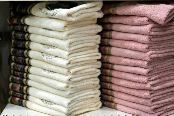 Δύο στοίβες λευκές και ροζ πετσέτες στο ράφι. Ράφια σε καταστήματα με πετσέτες terry διαφόρων χρωμάτων. Κοντινό πλάνο, Υφάσματα για το σπίτι, όμορφη Rolled λευκό πετσέτες μπάνιου σωρούς στο ράφι.  - Φωτογραφία, εικόνα