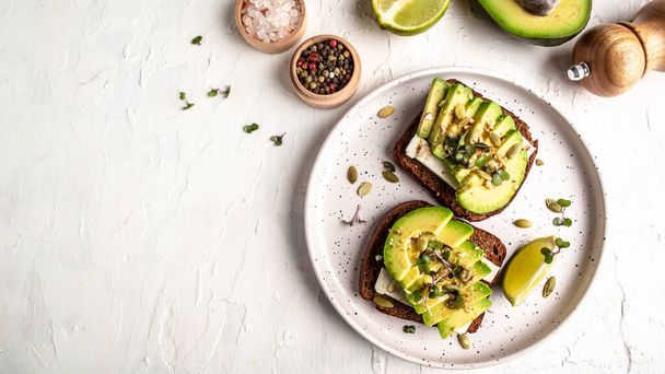 Healthy avocado toasts for breakfast or lunch with rye bread, sliced avocado, cheese, pumpkin and sesame seeds. banner, catering menu recipe top view. - Foto, Imagen