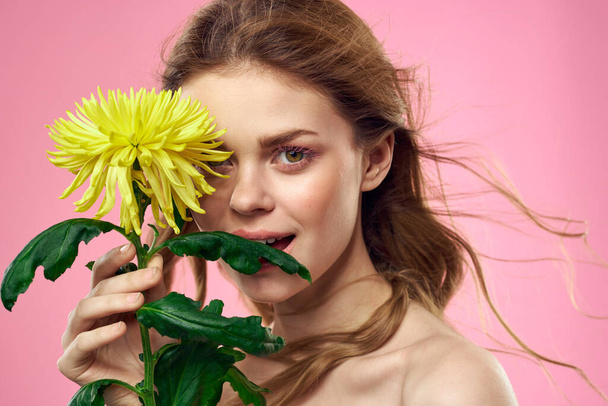 Retrato de una mujer con flores amarillas sobre un fondo rosa Maquillaje en la cara - Foto, Imagen