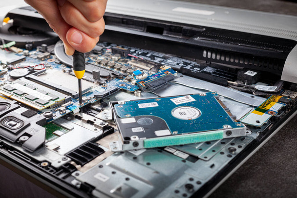 A computer technician is repairing an old laptop using a screw driver. Closeup isolated image showing complex interior of a laptop with circuit boards and delicate items. The person removes a screw. - Zdjęcie, obraz