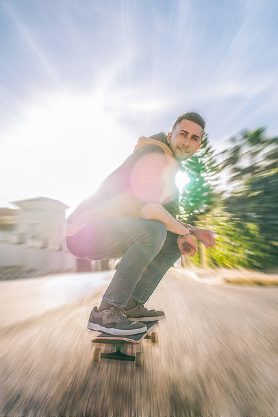 Молодой человек мчится по улице на скейтборде - Фото, изображение