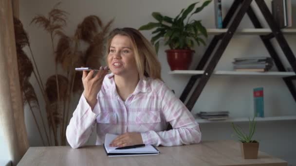 Χαρούμενη νεαρή λευκή κοπέλα ενεργοποιεί εικονική βοηθό σε ένα κινητό τηλέφωνο. Χαμογελαστή νεαρή Ευρωπαία που ηχογραφεί μια απάντηση σε ηχητικό μήνυμα σε ένα κοινωνικό δίκτυο για ένα φίλο  - Πλάνα, βίντεο