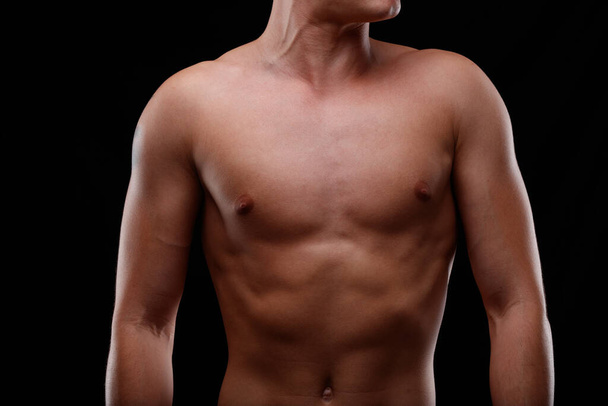 Nahaufnahme der nackten Brust eines athletisch durchtrainierten jungen Mannes vor schwarzem Hintergrund - Foto, Bild