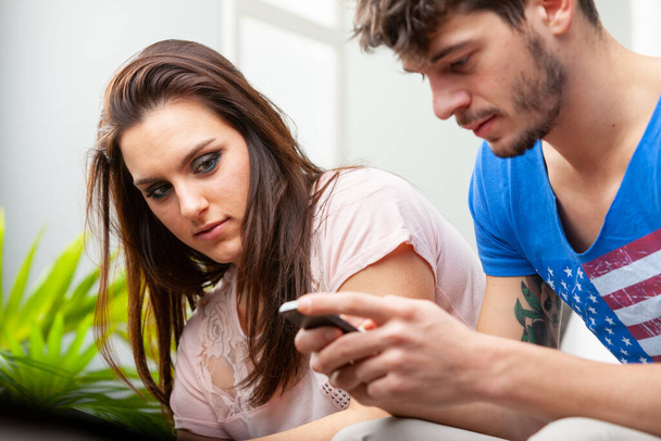 Mujer joven cuidadosamente mirando a su novio usando un teléfono móvil en una vista cercana más allá de sus manos a la cara - Foto, Imagen