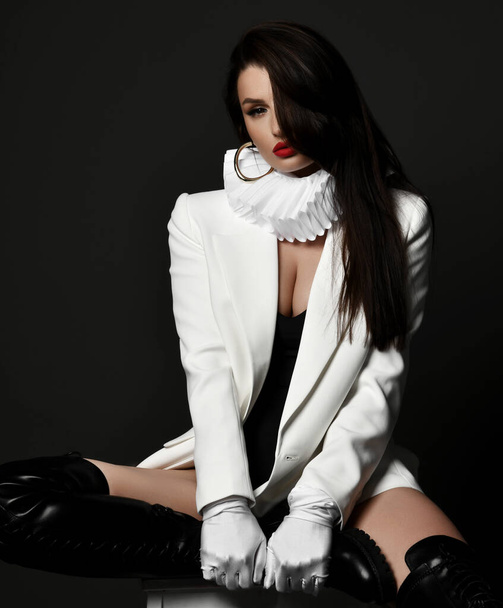 Sexy brunette pretty woman model in high boots, jacket and frill collar sitting on stool looking at camera - Фото, изображение