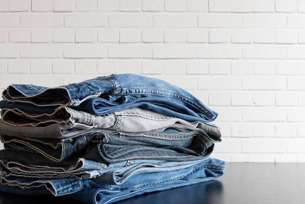 pile of folded jeans in front of white brick wall and on black background. Copy space.  - Valokuva, kuva
