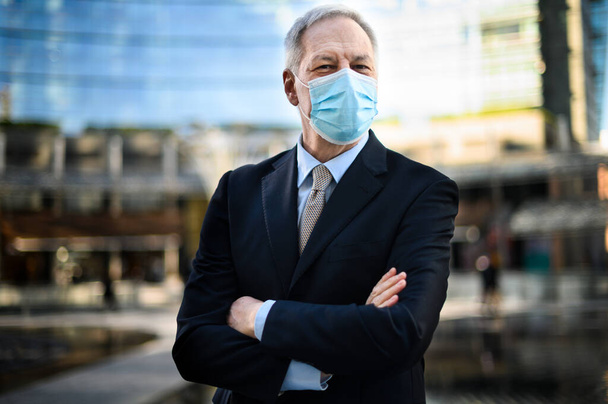 Senior manager with folded arms wearing a protective mask outdoor against Covid 19 - Fotografie, Obrázek