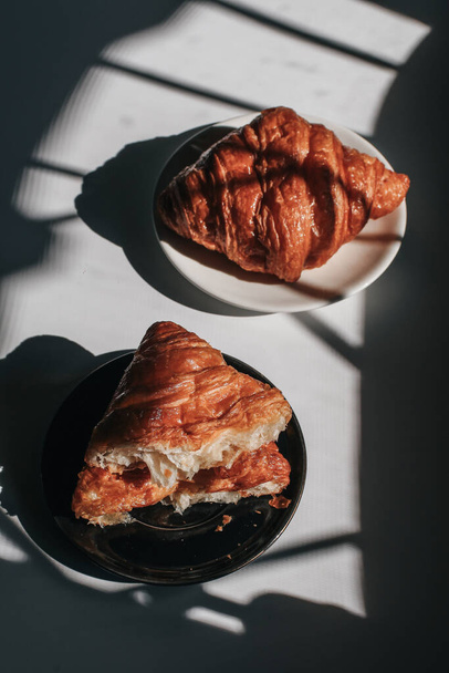 Croissants on a dark background in the morning light, sunlight shadow. Morning breakfast concept. Copy space. - Foto, Imagem