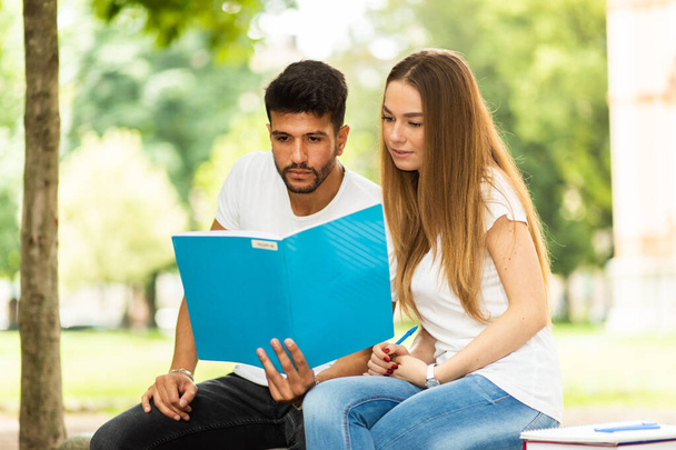 Two students studying together sitting on a bench outdoor - Foto, Imagem